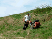 Dog Fence professional installing a dog fence on uneven ground, burying the cable with a trencher on a hillside."