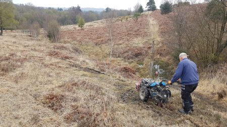A professional installing a dog fence on uneven ground, burying the boundary wire in a vast, sloped, and natural landscape."